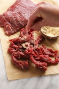 A person slicing beef on a cutting board for beef stroganoff.