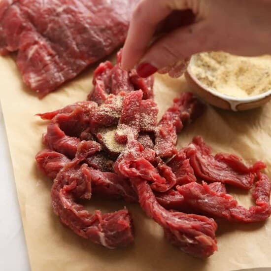 A person slicing beef on a cutting board for beef stroganoff.