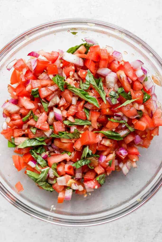 A bowl of bruschetta with fresh basil. 