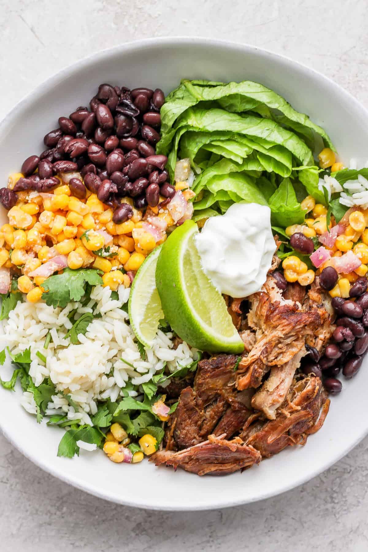 A bowl of slow cooker carnitas salad with corn, beans, and sour cream