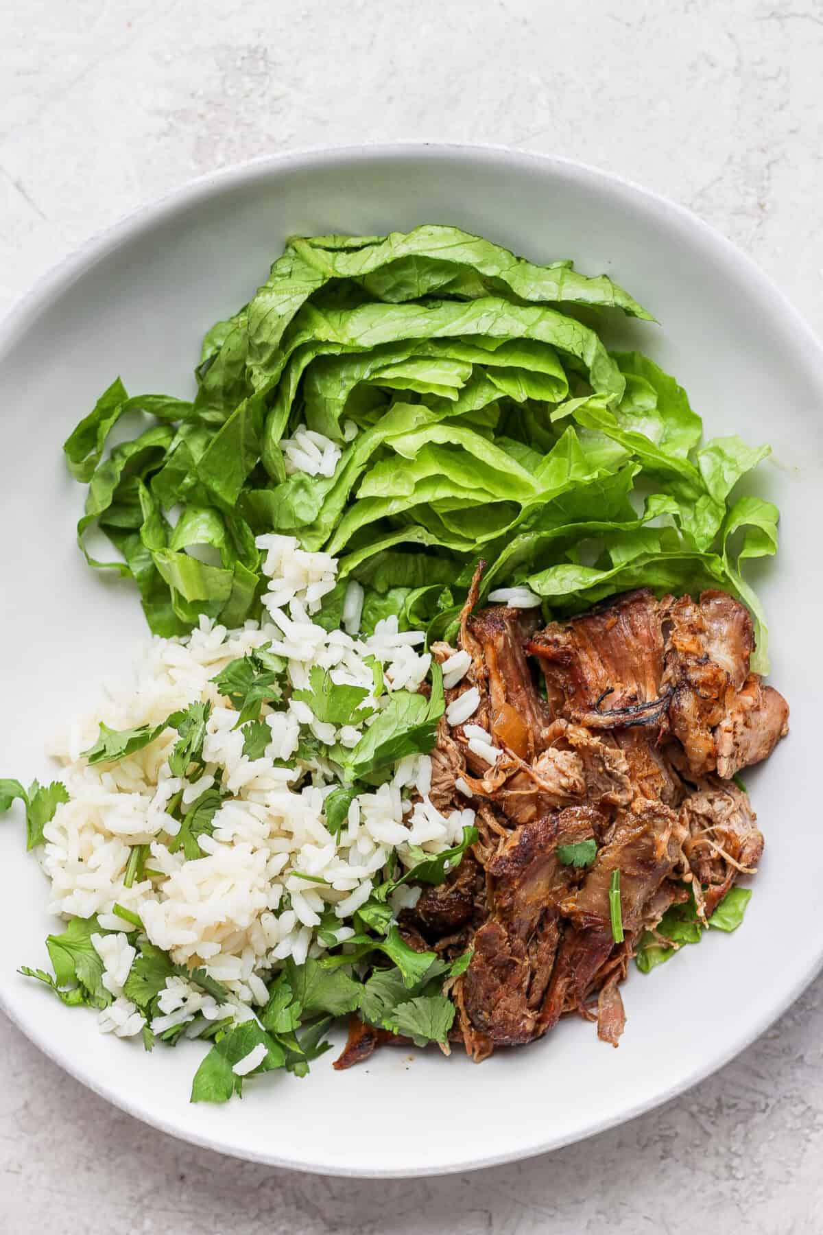 A white plate with slow cooker carnitas and greens.