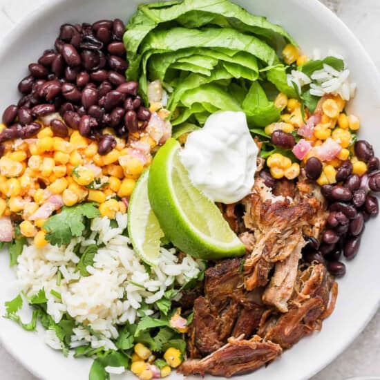 a bowl of mexican pulled pork salad with black beans, rice and sour cream.
