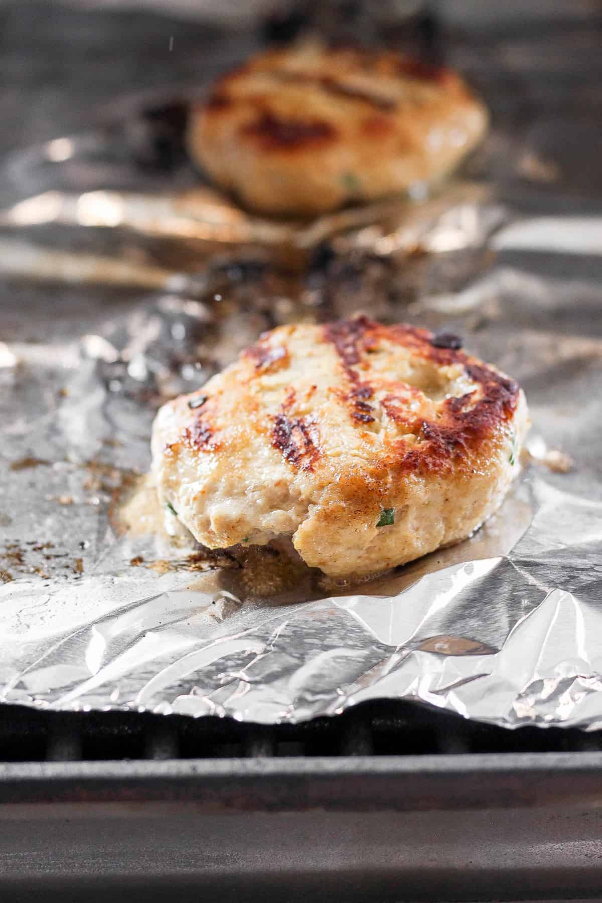 ground chicken burger on tin foil on grill.