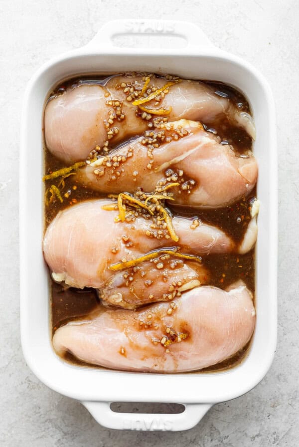 raw chicken in a white casserole dish with sesame seeds.
