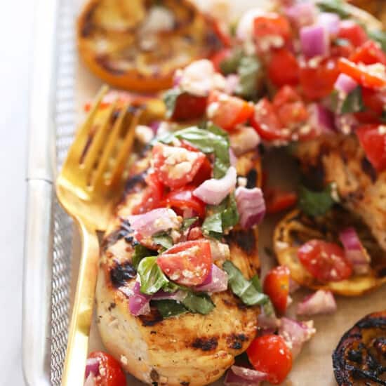 grilled chicken with tomatoes and onions on a baking sheet.