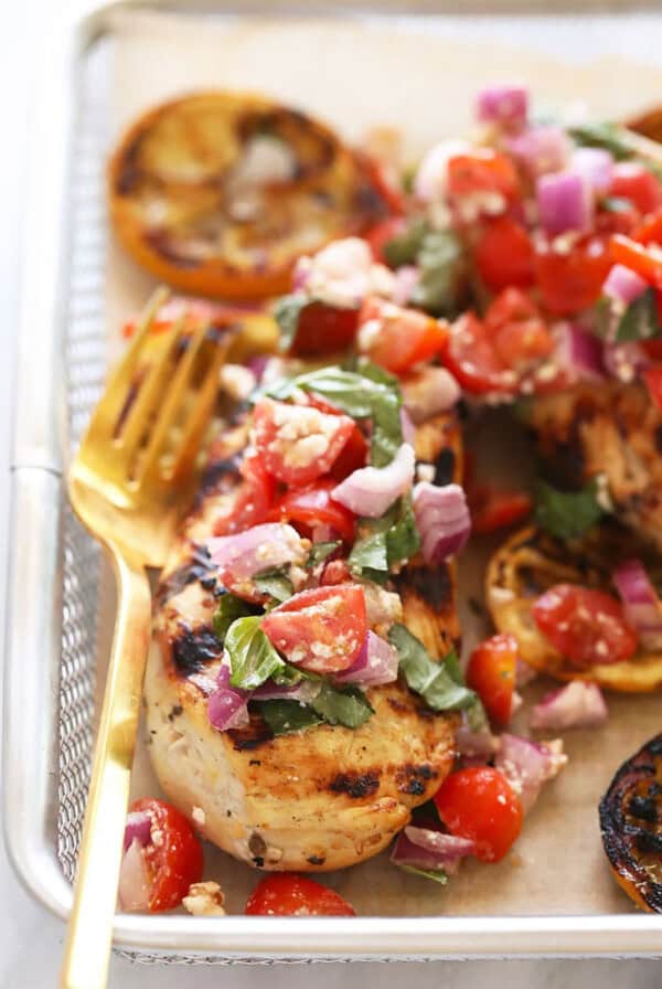 grilled chicken with tomatoes and onions on a baking sheet.