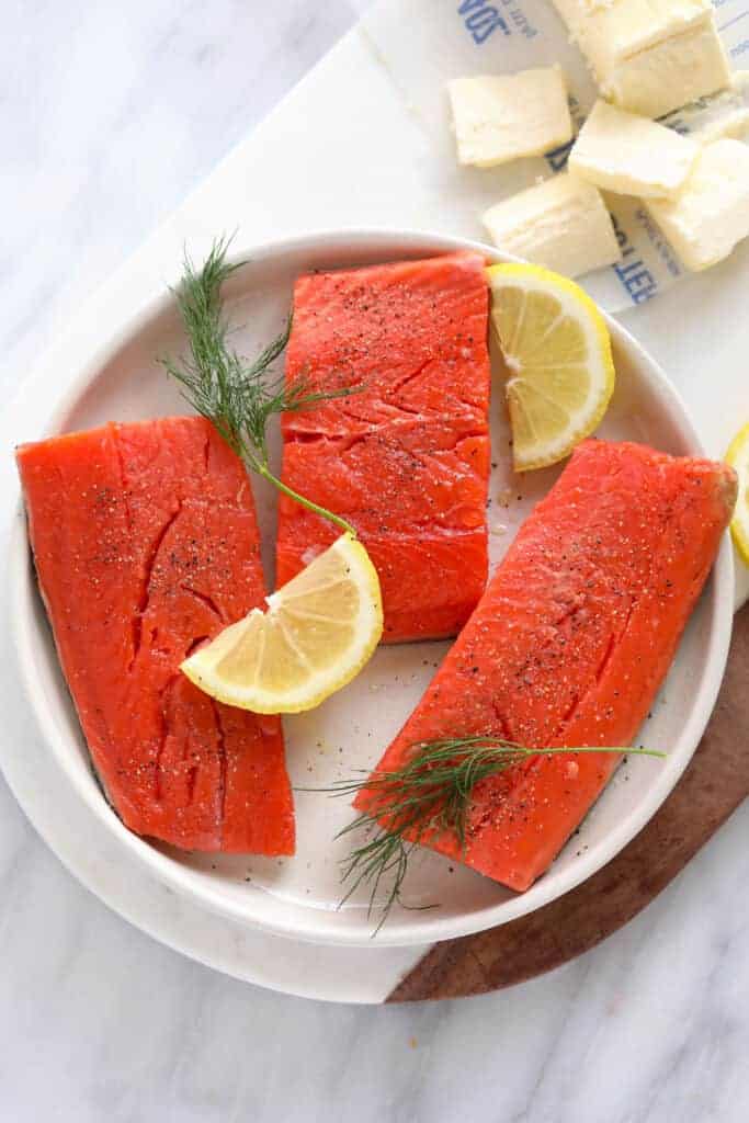 uncooked salmon fillets with lemon and dill on plate.