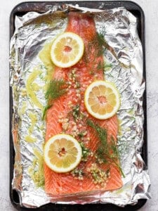 salmon on top of foil with dill and lemons.