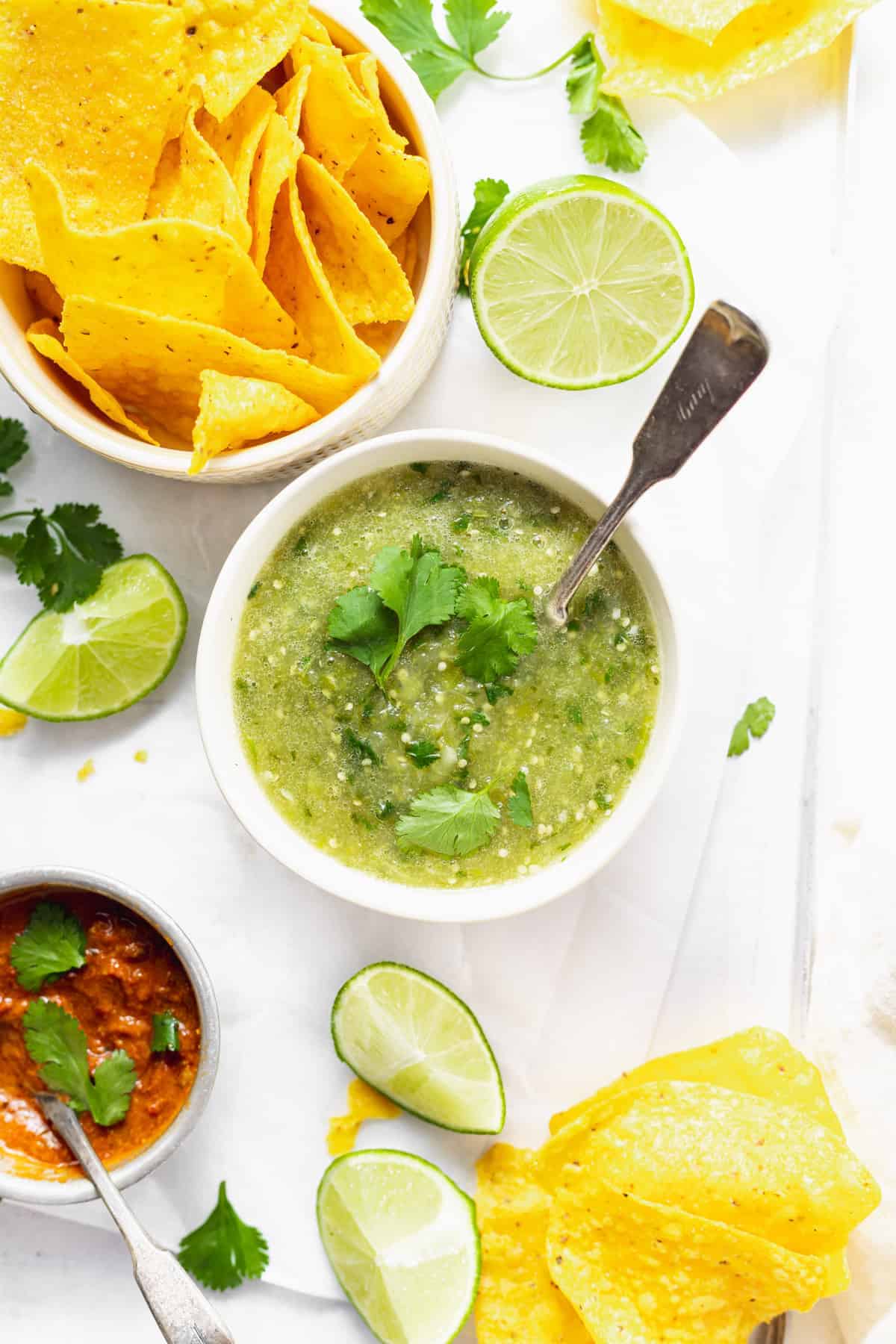 Salsa verde in a bowl surrounded by chips and lime wedges. 