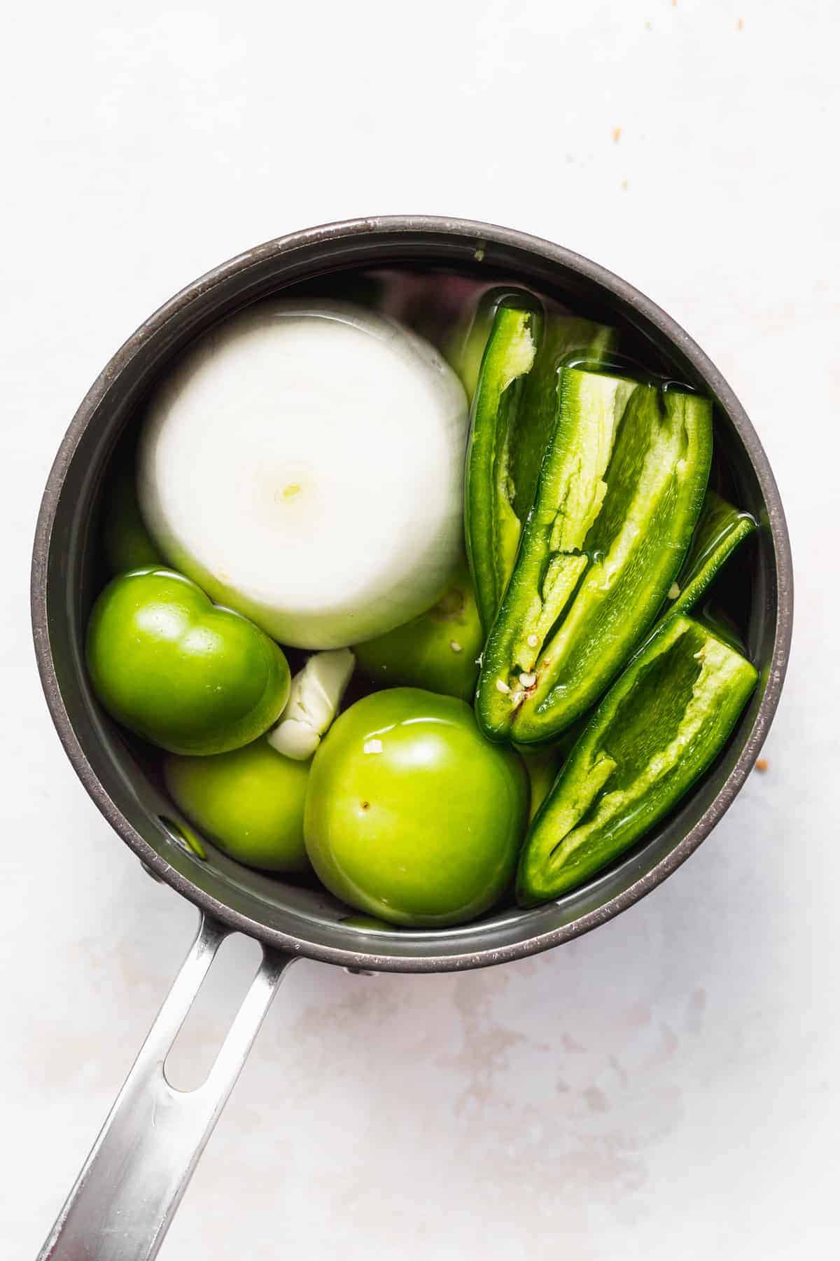 Tomatillos, garlic, onion, jalpeños, and other ingredients in a saucepan. 