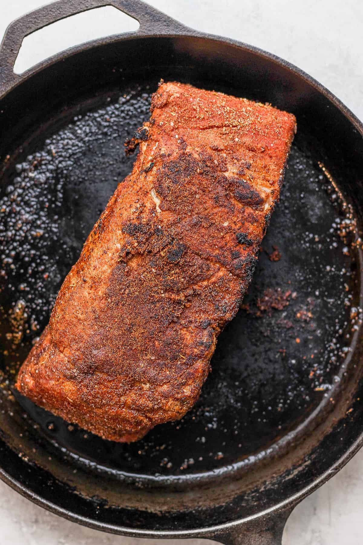 Pork shoulder being seared in a cast iron. 