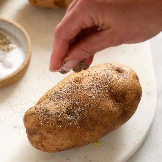 a person is sprinkling salt on some potatoes.