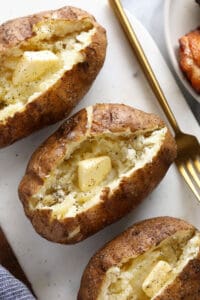 three baked potatoes on a plate with a fork.