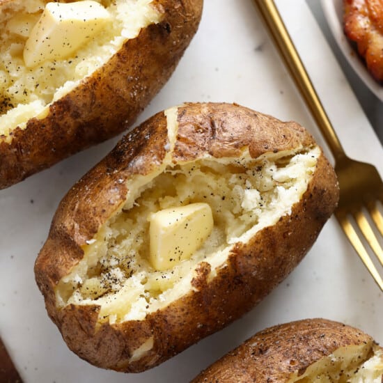 three baked potatoes on a plate with a fork.