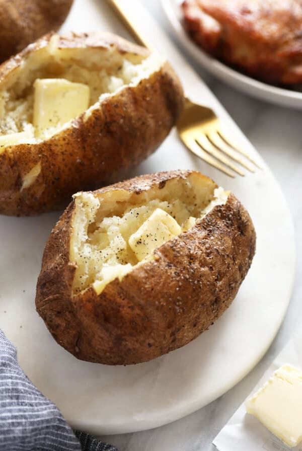 three baked potatoes with butter on a white plate.
