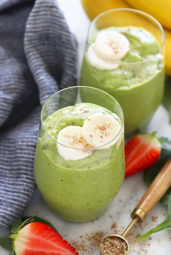 two glasses of green smoothie with bananas and strawberries.