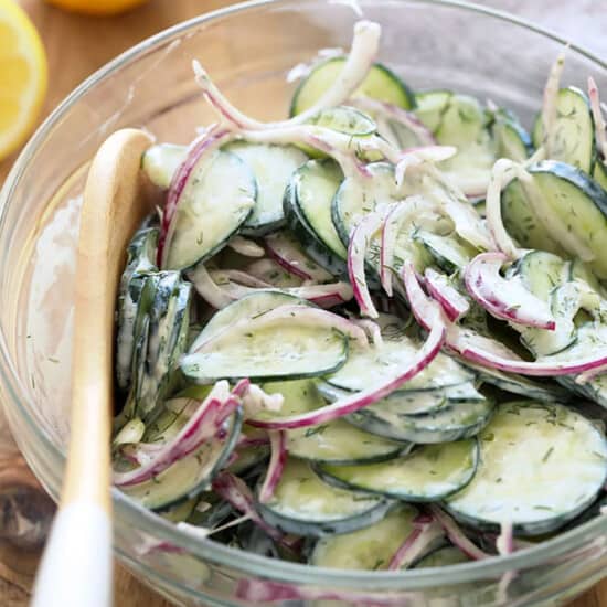 a bowl of cucumber and onion salad with a wooden spoon.