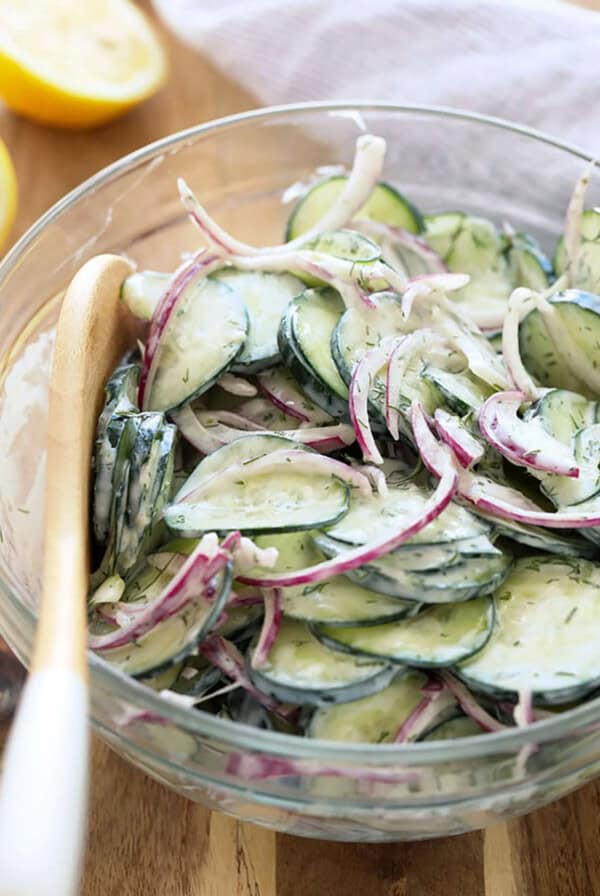 a bowl of cucumber and onion salad with a wooden spoon.