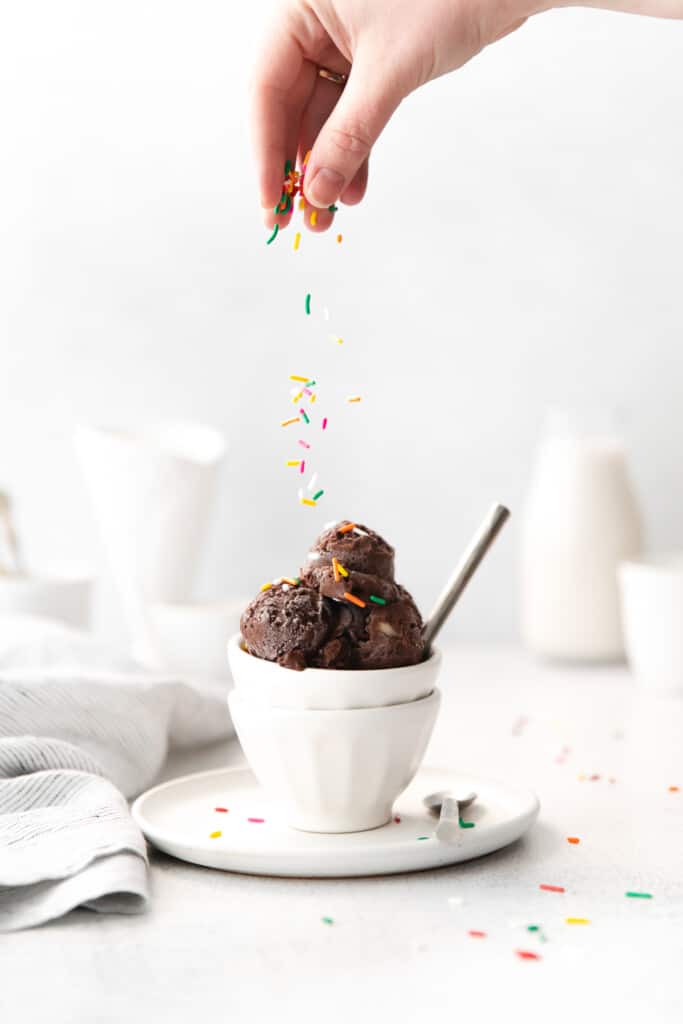 Sprinkling sprinkles on top of chocolate protein ice cream.
