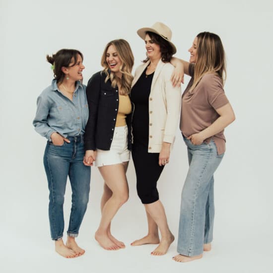 four women posing for a photo in front of a white background.