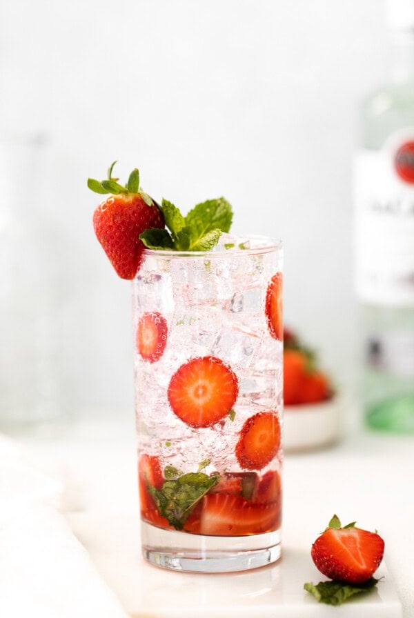 a glass of gin and tonic with strawberries and mint.