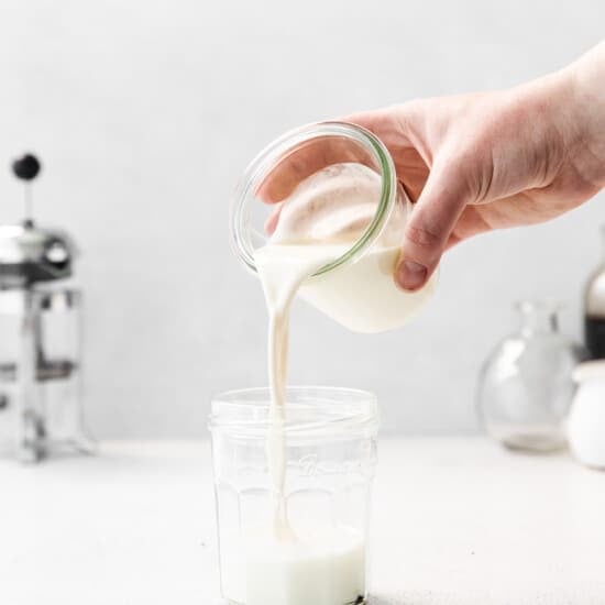 a hand pouring milk into a glass jar.