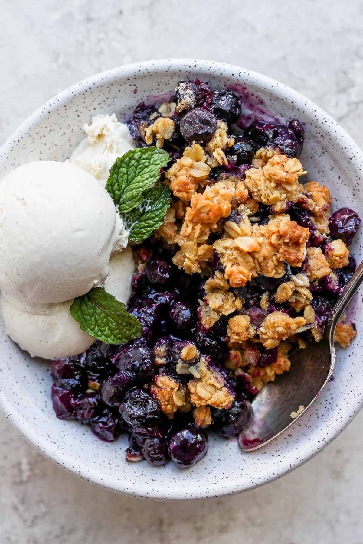 A bowl of blueberry crisp with ice cream. 