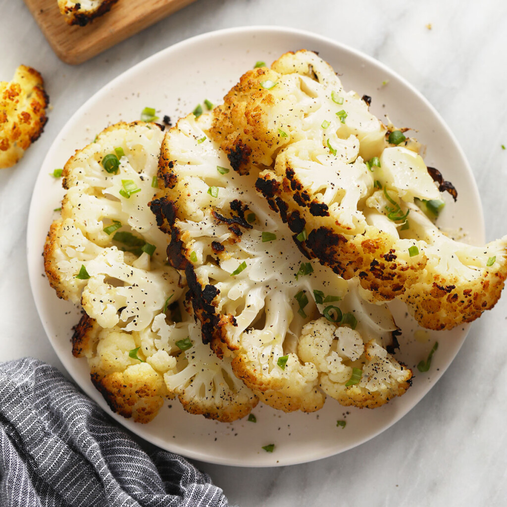 a white plate topped with cauliflower next to a cutting board.