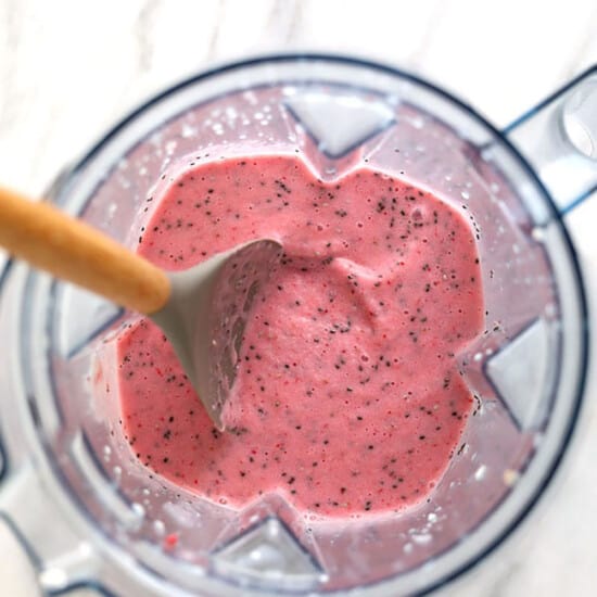 a blender filled with a pink smoothie with a wooden spoon.