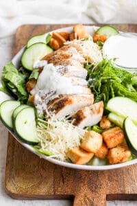 a chicken salad with croutons and dressing on a wooden cutting board.