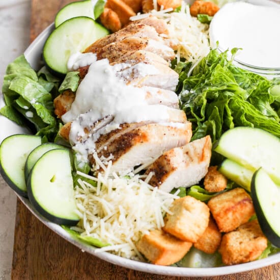 a chicken salad with croutons and dressing on a wooden cutting board.