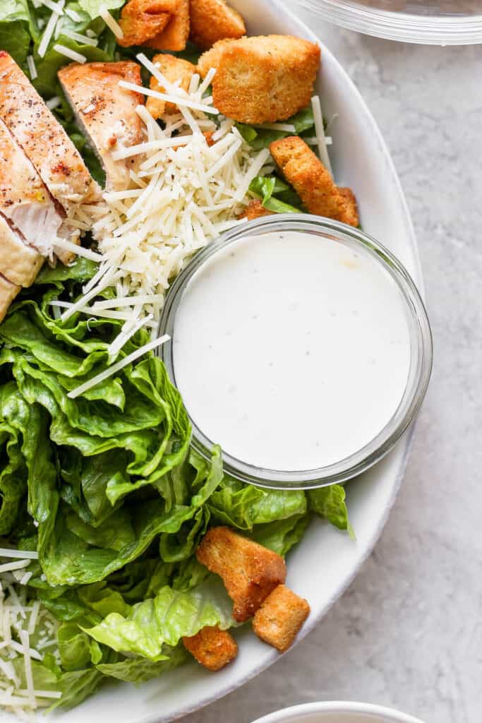 A chicken caesar salad with a bowl of dressing on the side. 