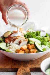 Pouring caesar dressing over a salad.