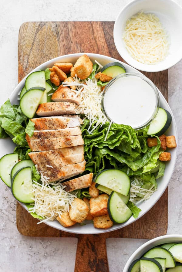 a salad with chicken and cucumbers on a wooden cutting board.