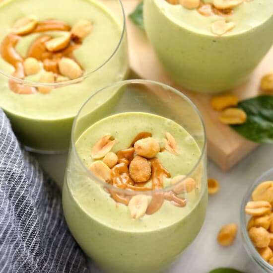 two glasses of green smoothie with peanuts and green leaves.