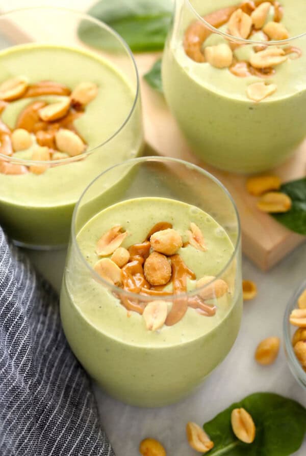 two glasses of green smoothie with peanuts and green leaves.