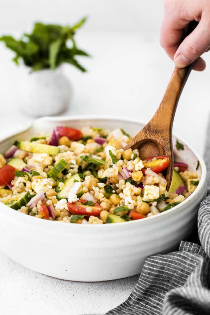 mediterranean couscous salad in a bowl being stirred with a spoon