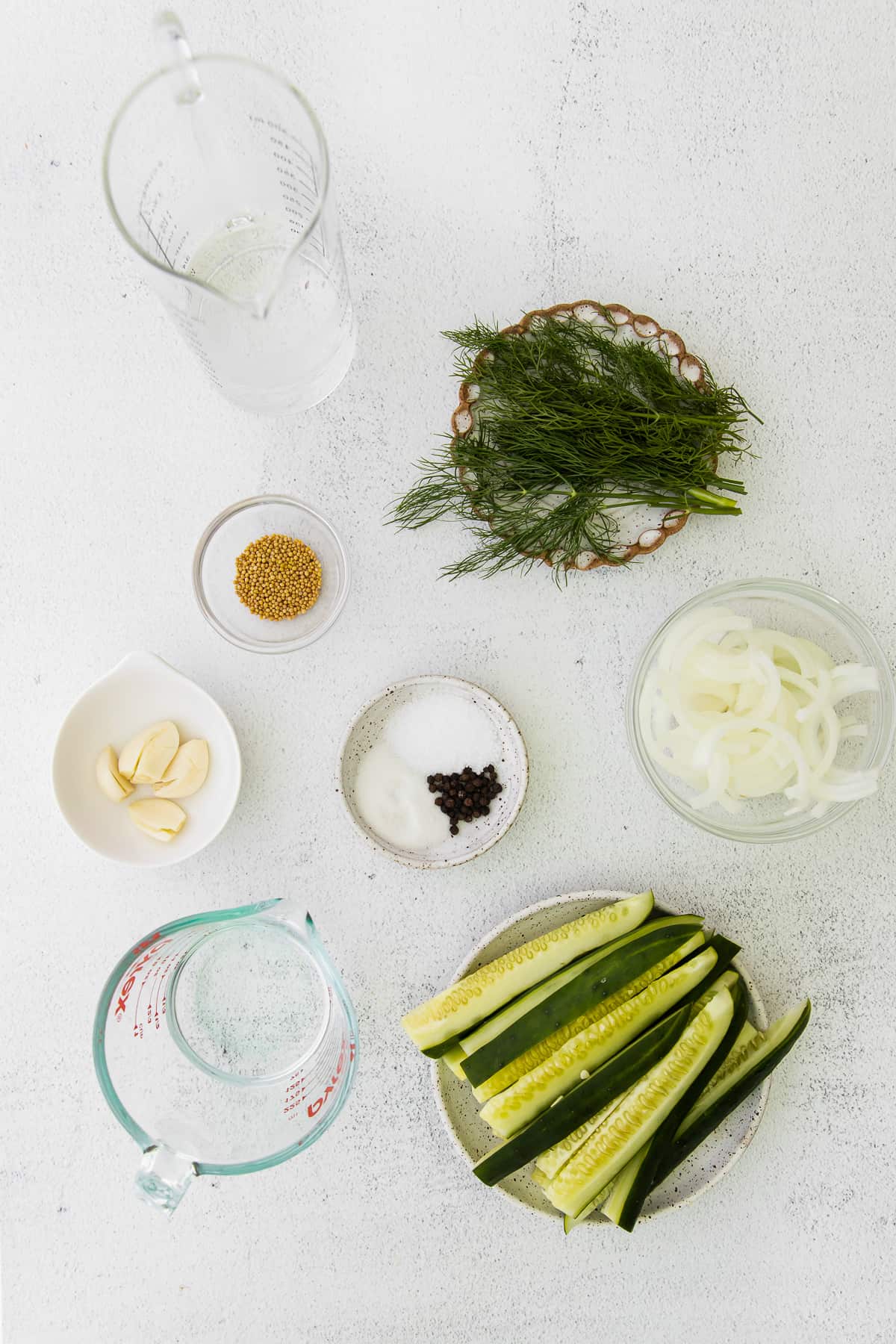 Sliced cucumbers, fresh dill, white onion, mustard seeds, sugar, garlic, and vinegar on the counter top. 