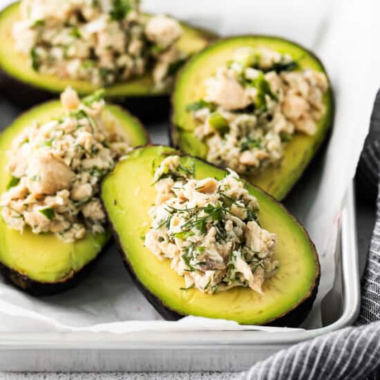 Stuffed avocados with tuna and herbs on a baking sheet.