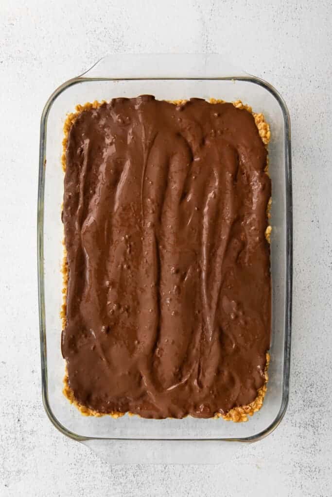 These healthy Scotcheroos are made with all-natural sugar, unsalted peanut butter, and coconut oil (no white sugar or corn syrup)! They're ready in no time and are a great healthy twist on this classic dessert bar. Melted chocolate layer of healthy Scotcheroos in a casserole dish