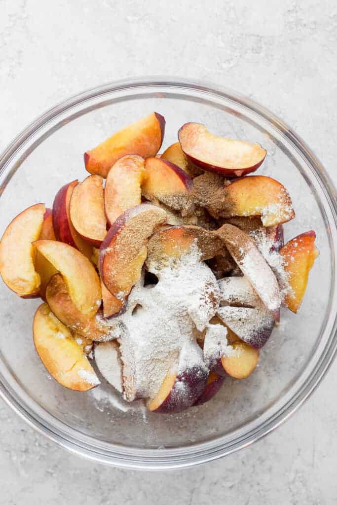 Sliced peaches in a bowl topped with flour and ،es.