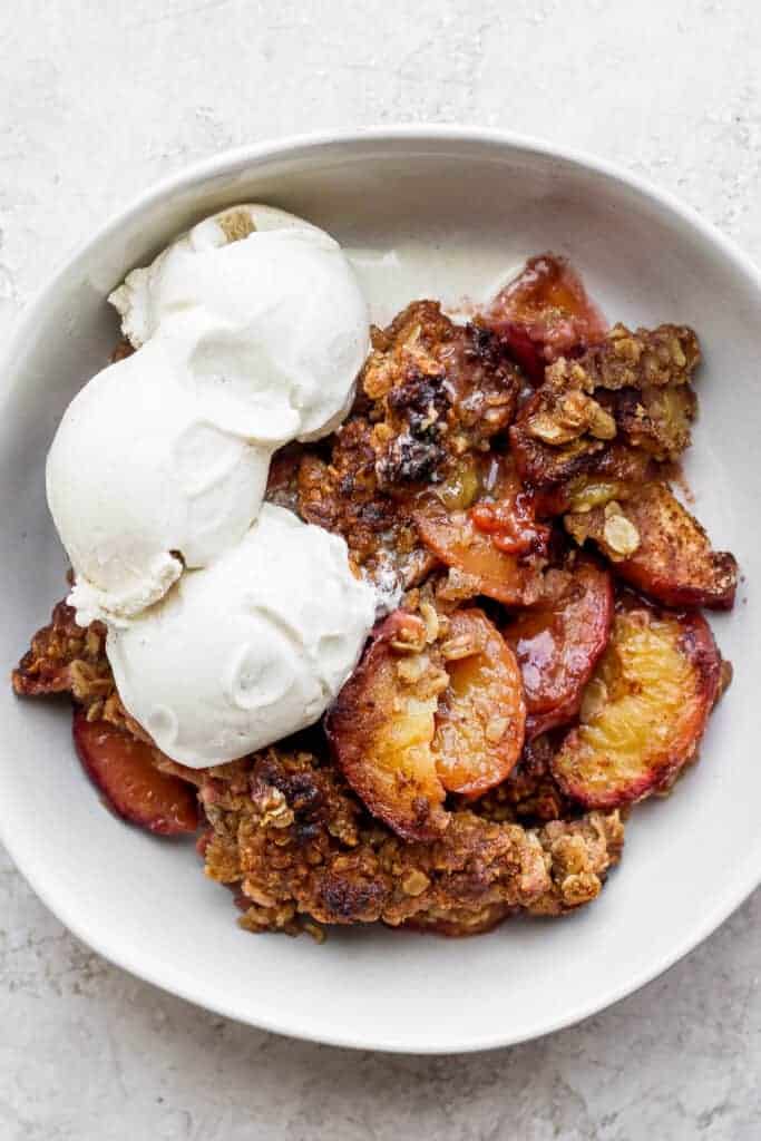 Peach crisp in a bowl with vanilla ice cream.