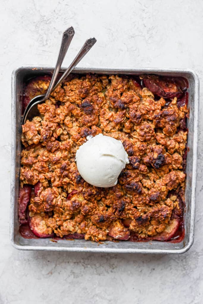 Peach crisp topped with a scoop of vanilla ice cream in a square baking dish.