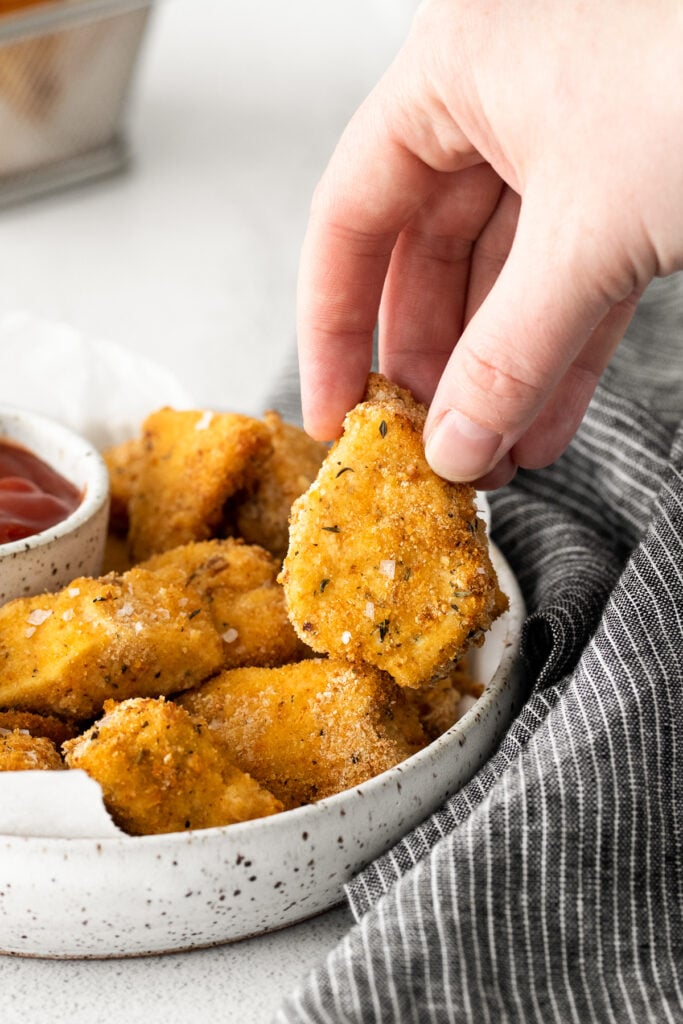 A hand ،lding an air fryer chicken nugget. 