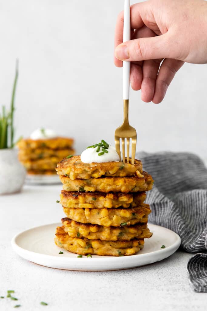 A stack of corn fritters with Greek yogurt and chives sprinkled on top. 