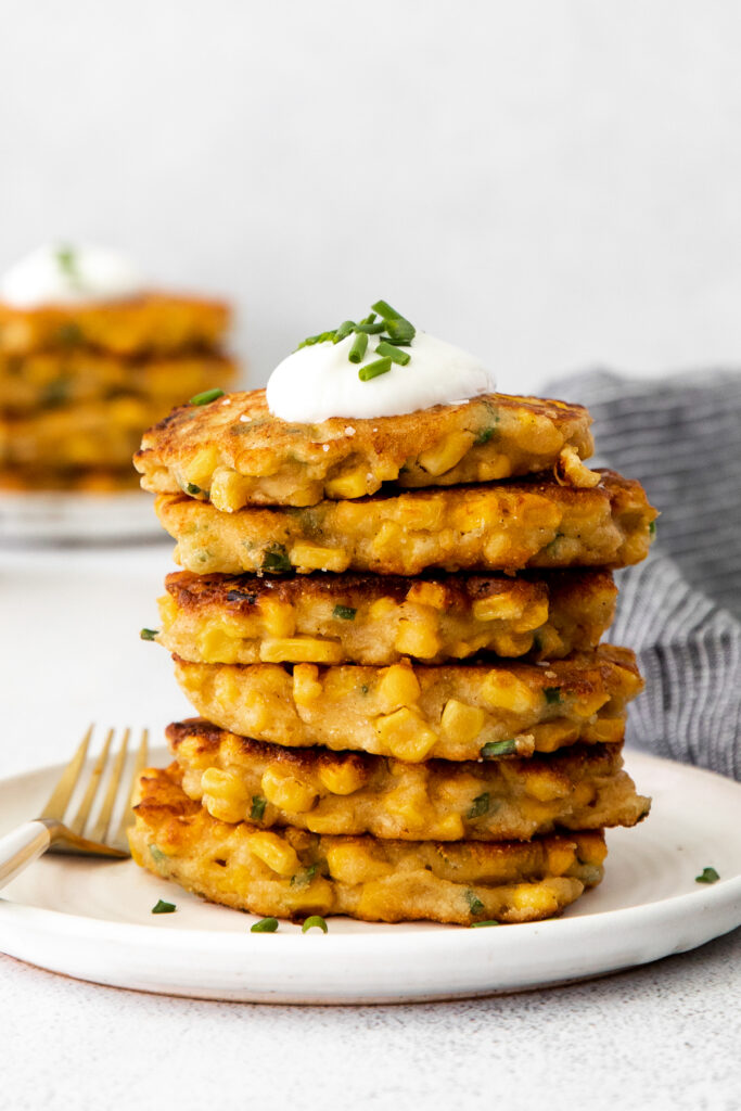 A stack of corn fritters with Greek yogurt and chives on top. 