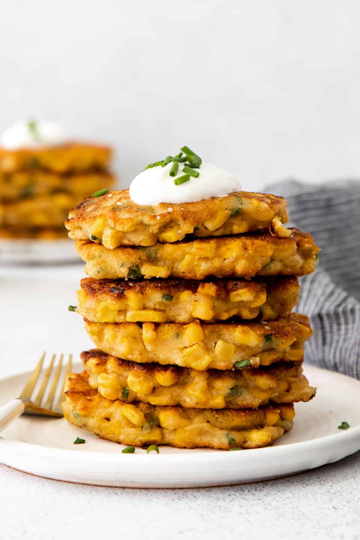 A stack of corn fritters with Greek yogurt and chives on top. 