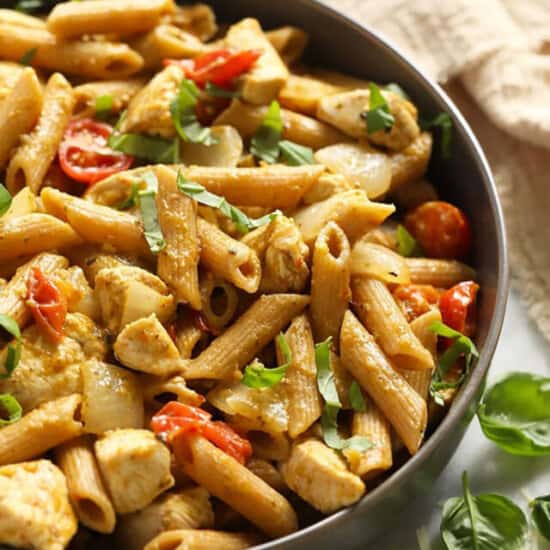 A bowl of pasta with chicken and tomatoes.