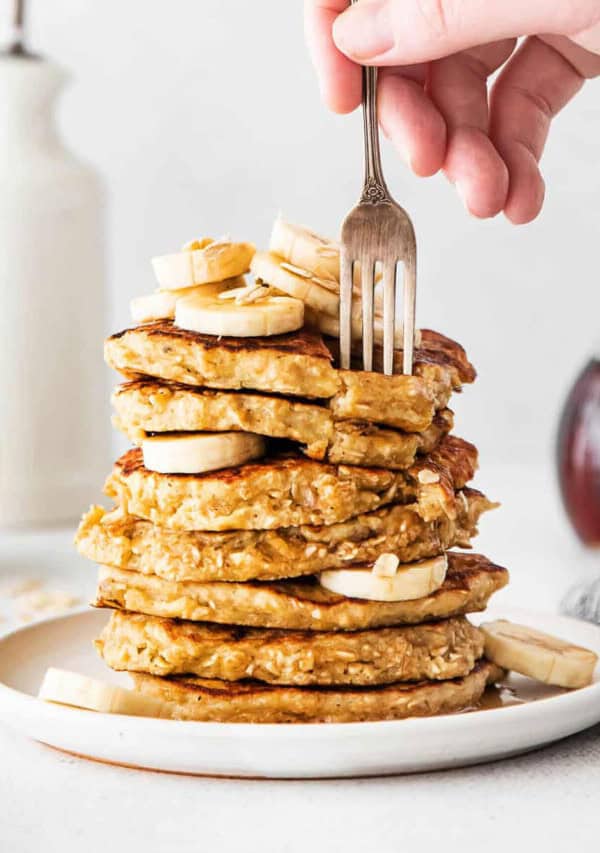 A stack of pancakes with bananas and syrup on a plate.