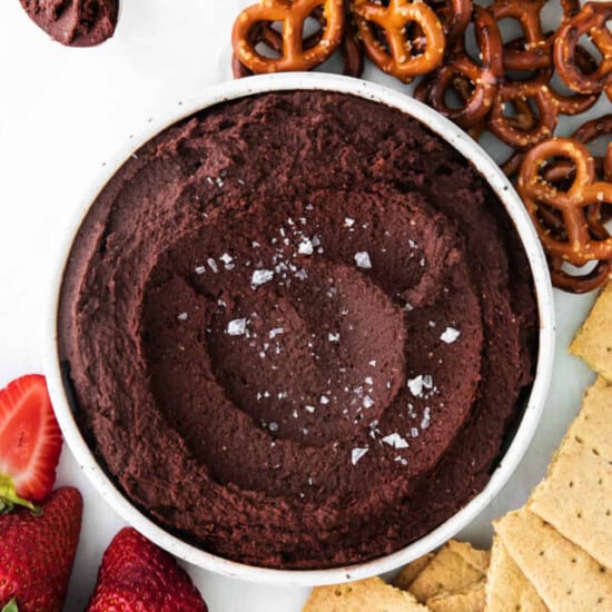 A bowl of chocolate hummus with strawberries and pretzels.